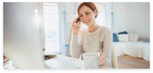 A woman answering a telephone call while holding a cup of coffee